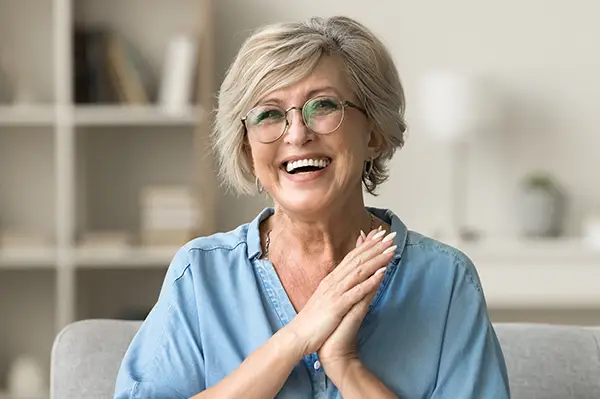 Cheerful pretty older woman in elegant glasses sitting on cozy home couch at Picasso Dental Care in Temecula, CA
