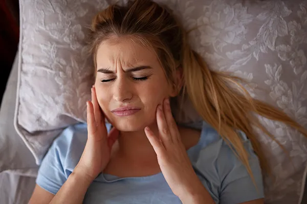 Woman suffering from bruxism and rubbing her jaw while in bed.Picasso Dental Care in Temecula, CA 