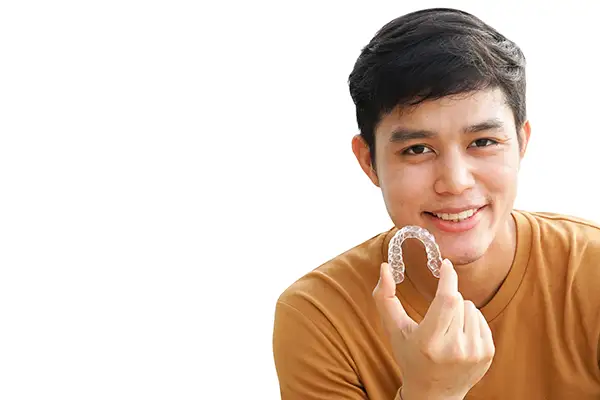 Smiling teenage boy holding a clear aligner in his hand, demonstrating its use as an alternative to traditional braces.